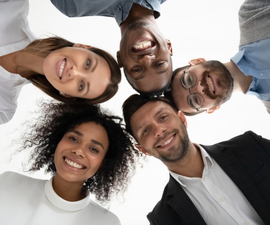 Small group of young adults with their heads together in a circle looking down at the camera